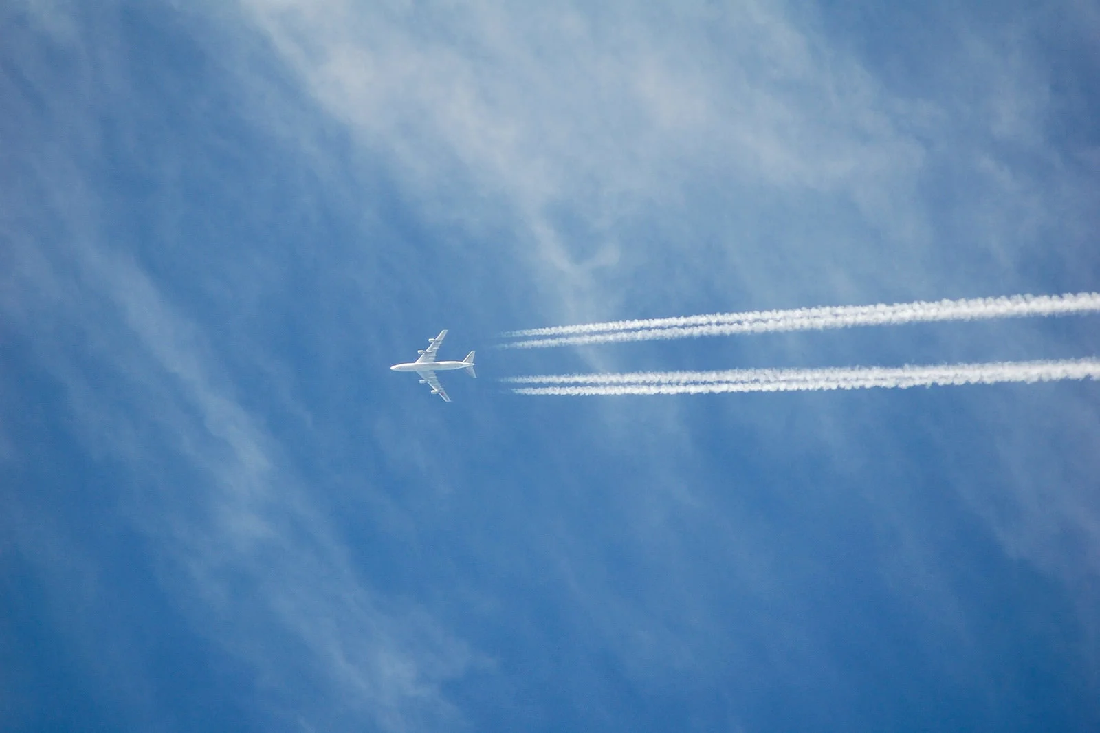 青空を飛ぶ旅客機と、機体後方に伸びる2本の白い飛行機雲